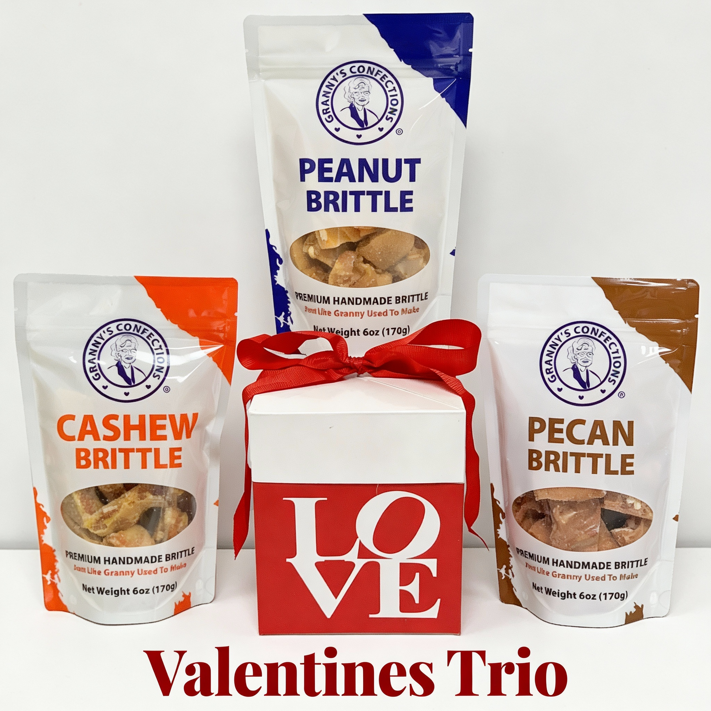 Three bags of brittle with a 'LOVE' box on a white background, labeled 'Valentines Trio'. peanut, cashew, pecan